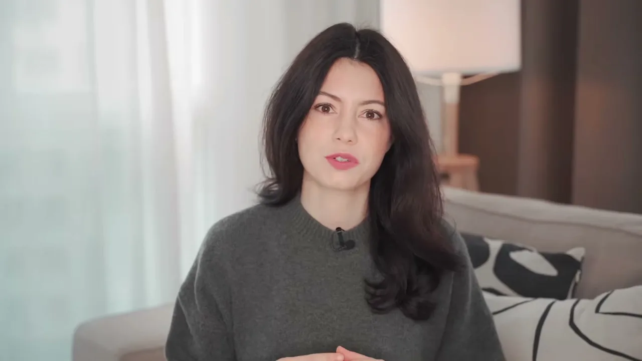 A creator in a grey sweater talking to the camera on a sofa in soft window light