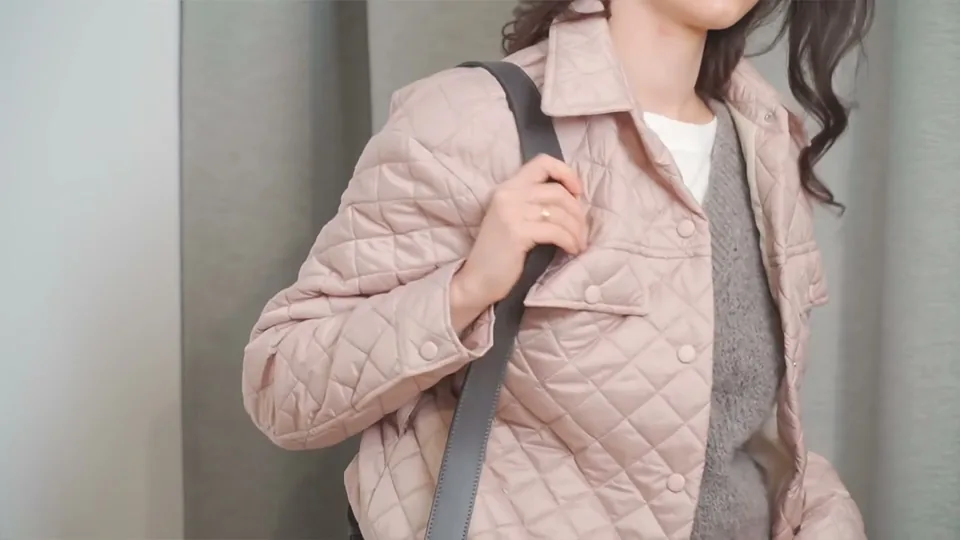 Close-up of a pink quilted jacket with a grey bag strap over the shoulder