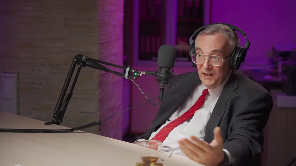 A guest in a suit and red tie speaking at the table, April 2021