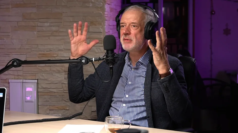 The guest's close-up: a physicist in headphones explaining something with both hands raised