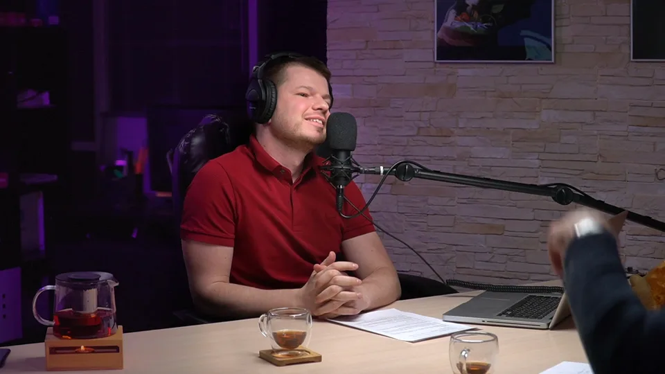 The host's close-up: a man in a red shirt and headphones listening at the table