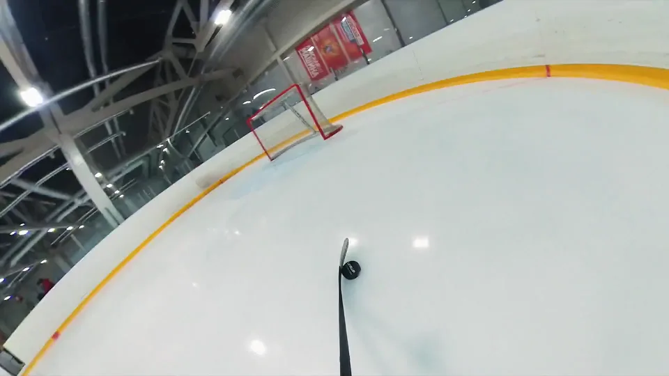 An FPV drone shot low over the ice: the puck in front of the stick and the goal ahead