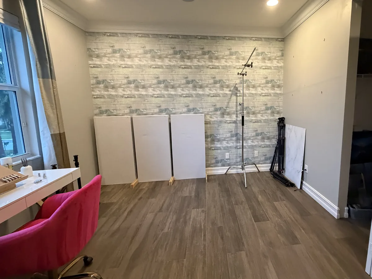 Before: the same room as a home office with wood-look wallpaper, a desk and panels leaning on the wall
